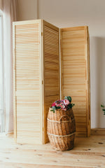 Light wooden slatted room divider with a basket in front filled with pink flowers.