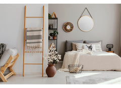Bedroom in a simple design, in the forefront of the photos is a ladder with a blanket drooped over it.
