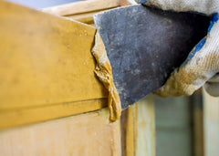 Close up of a hand with a scraper removing paint from wood