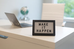 Close up image of a desk with a sign that says, "Make it happen"
