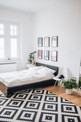 White and bright bedroom, bed with white bedding.  Black and white rug on the floor.