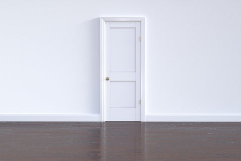 White wall with nothing but a white door, hardwood floors.  Entire room is empty