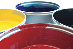 Close up of the tops of paint cans, showing red, yellow, blue and black paint