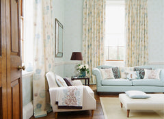 A light blue living room with more traditional looking furniture, curtains that hang from almost the ceiling to floor length.