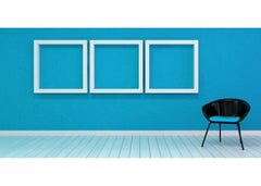 Room with white floors, teal wall and on the wall are 3 large white frames that are empty.  There is a single black chair in front of the wall.