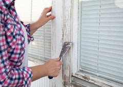 Woman removing trim paint from a window.