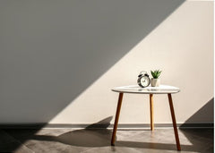 Accent table in front of a blank wall.  There is a plant and a clock sitting on the table.