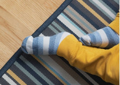 Close up of baby feet in yellow sweatpants and blue and white striped socks.  Baby is sitting on the a striped rug on a light wood floor.