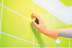 Bright yellow green wall tile, someone is wearing an orange glove and cleaning it with a sponge.