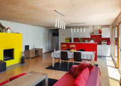 Open living room to dining room and kitchen.  Fireplace is painted bright yellow, sofa is red and there are red accents in the kitchen.