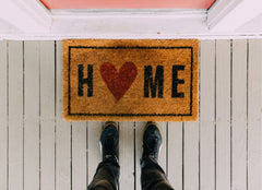 Looking down at a door mat that says, "Home" in front of a door.