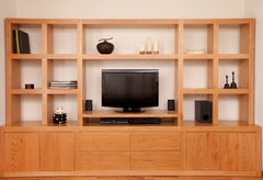 Light wood entertainment center with cabinets below and square shelving above with the television in the center.