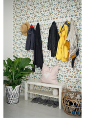 Entry wall with wallpaper, wall hooks with hanging coats, bench below with shoes on it.