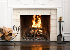 Fireplace with a fire going, a stack of wood on the left side and fireplace tools on the right side.