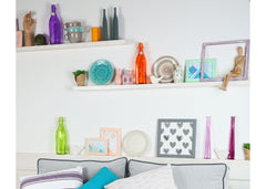 Floating shelves above a sofa with fun colored bottles and various items.