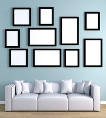 blue wall with a white sofa in front and the wall above is filled with various black frames.