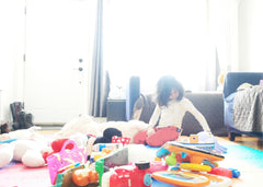 Little girl playing on the floor in a living room surrounded by a lot of toys