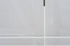 Close up of gray tiles with white grout, grout is missing at the top of the vertical line.