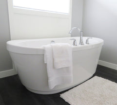 Modern white tub with a white rug in front of it on the floor.