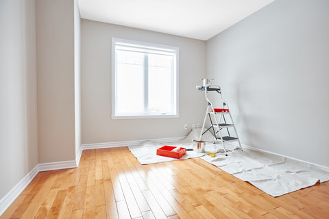 Empty room with wood floors, drop cloth and ladder as if someone is prepping for painting.