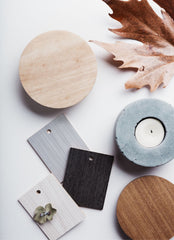 White background, some laminate samples in gray and black, a wood sample, and a leaf as well as a round concrete candle holder with a candle in it.