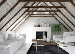 Simple living room set within an attic space with sharp angled roof and wooden beams.  All of the furniture is white, except for the rug which is black.