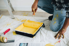 Man bending down to get yellow paint on a roller to paint a wall.