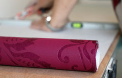 Magenta roll of wallpaper, a hand is rolling it out.