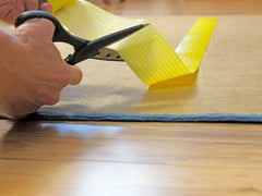 Hand cutting yellow rug tape on the backside of a rug.