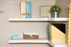 White corner floating shelves with some books and art on them.