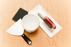 Photo of putty, putty knife, sandpaper all sitting on the floor.