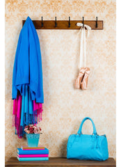 Wall papered wall with a blue coat hanging on wall hooks as well as ballerina slippers, bench below with books and a plant.