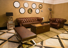 Beige living room with oversized leather sofas and behind the large sofa is a grouping of mirrors