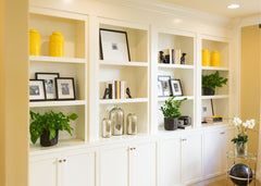 Built in shelves with cabinets below.  Artwork, books and yellow accent vases sit on the shelves.