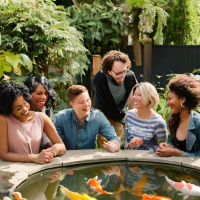 A diverse group of friends enjoying a koi pond in a garden.