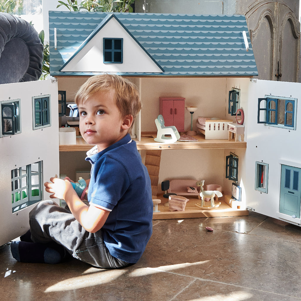 A boy playing at a large wooden doll's house