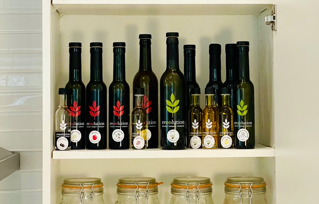 A white cupboard is filled with Evoolution bottles of olive oil and balsamic vinegar. 