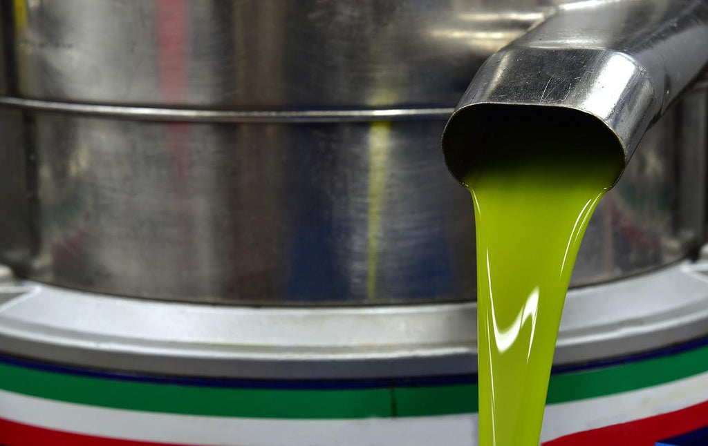 Bright green olive oil is poured from a stainless steel vessel.