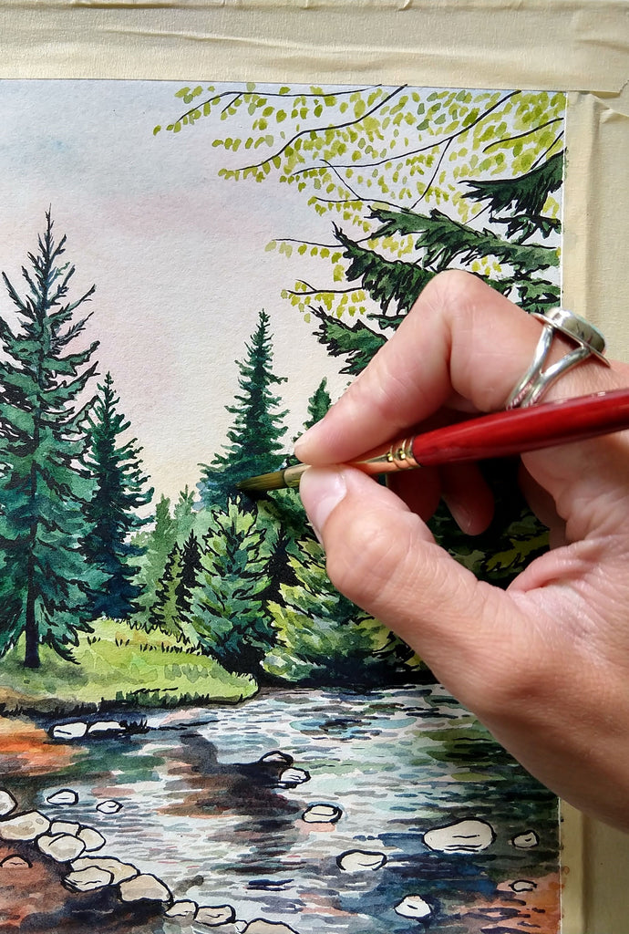 Hand holding a paint brush and painting a pine tree