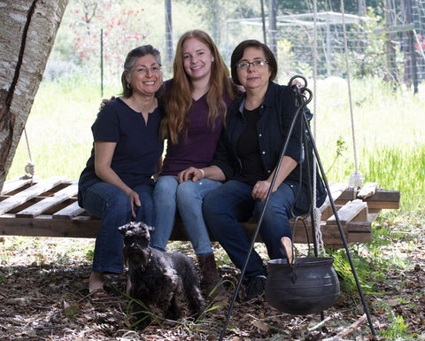 Owner Emma her sister and daughter sitting outside on a large pallet swing with a small black dog and black cauldron in foreground