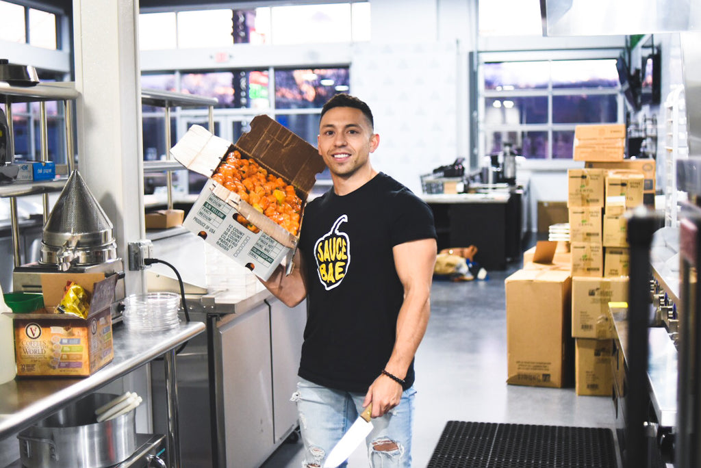 Founder of Sauce Bae Kevin Carbone in a commercial Kitchen holding habanero peppers and wearing a Sauce Bae shirt