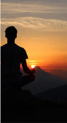 Male meditating on a mountain at sunset