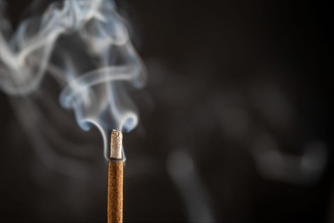 A close up image of a burning incense stick letting off smoke.