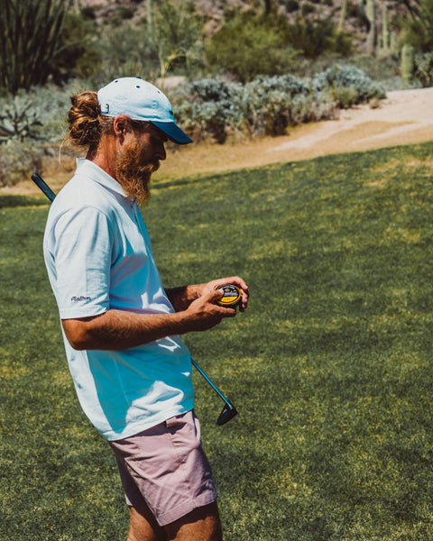 Golfer on a golf course looking at and holding a Cannadips CBD Tropical Mango can.