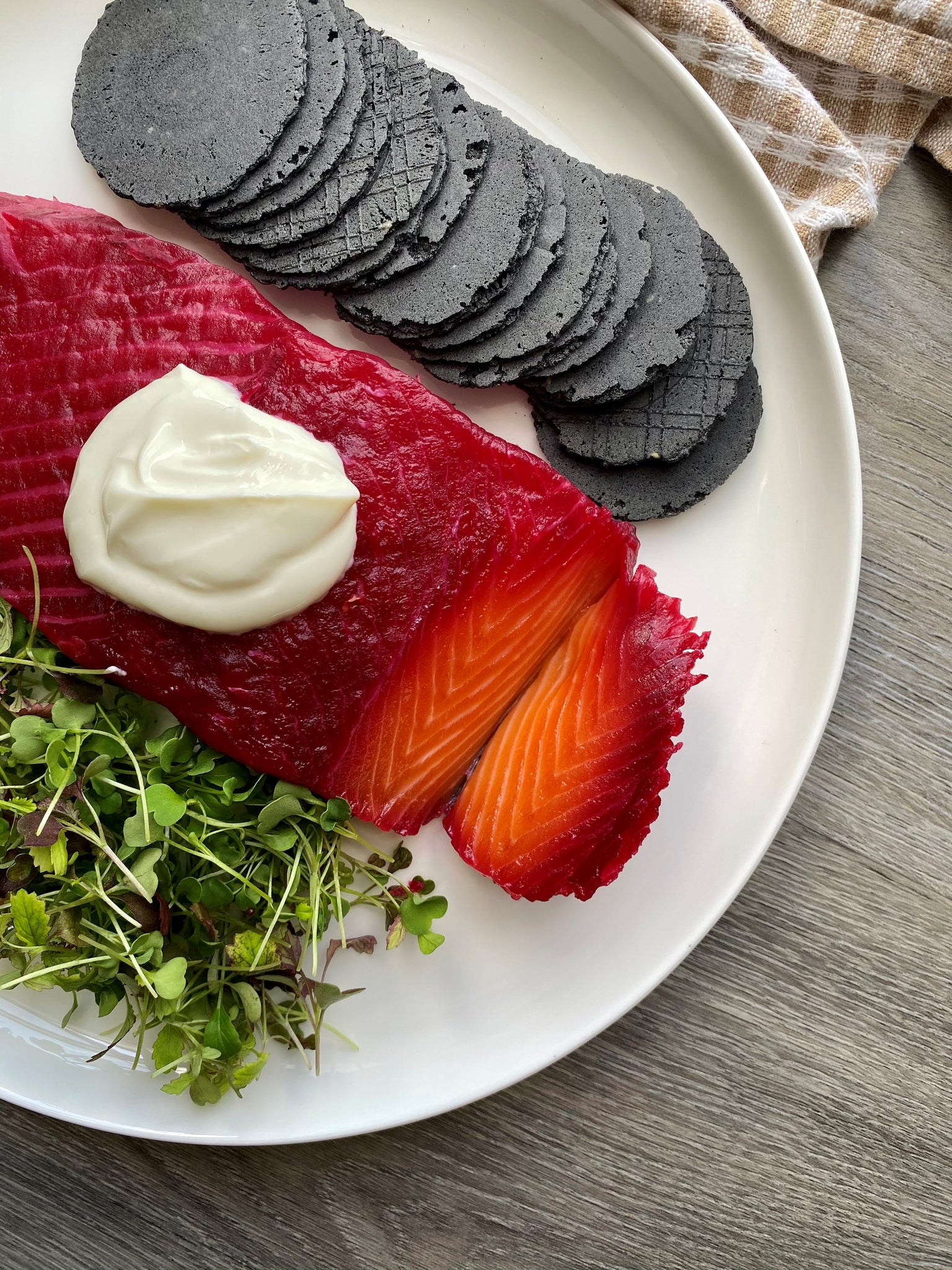Beetroot cured salmon on a plate with charcoal crackers and microgreens