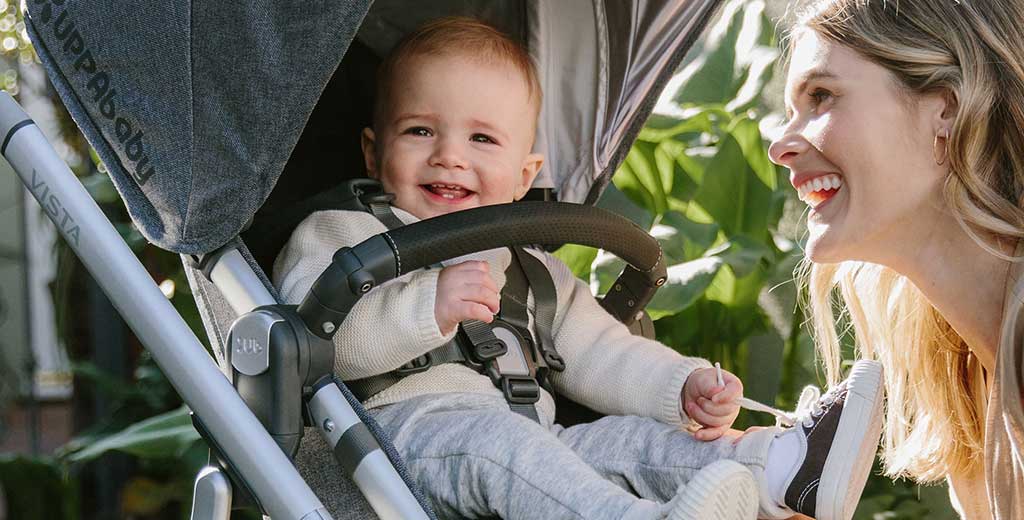 Happy baby in an Uppababy stroller with mom smiling nearby.