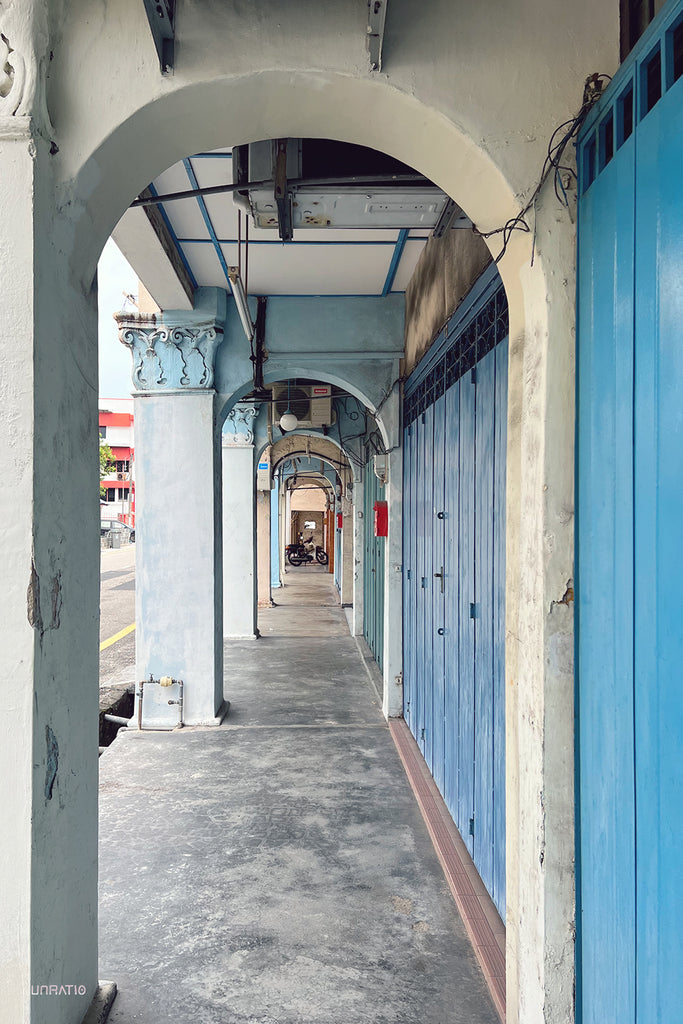 Arched colonial walkway with blue wooden doors in Melaka, reflecting traditional Malaysian architectural style.