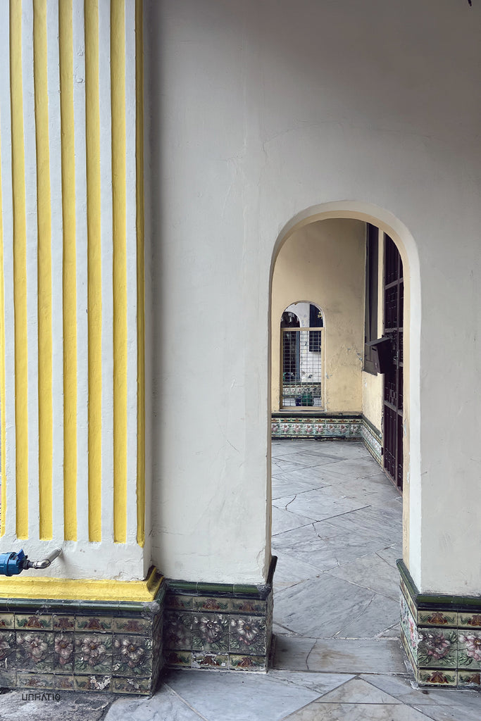 Arched passageway along a street in Melaka, with striking yellow pillars and decorative tiled base, evoking historical charm.