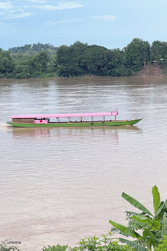 Serene Mekong River cruise with a traditional longtail boat adorned with a vibrant pink canopy, reflecting the peaceful river life in Chiang Khan, Thailand.