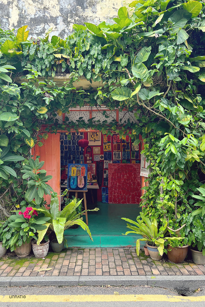 Vibrant art gallery entrance in Melaka, enveloped by lush tropical plants and a colorful doorway.